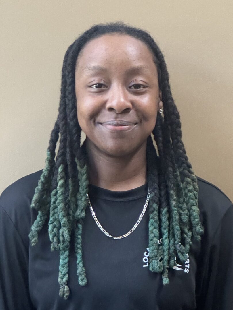 A woman with long braids wearing black shirt and smiling.